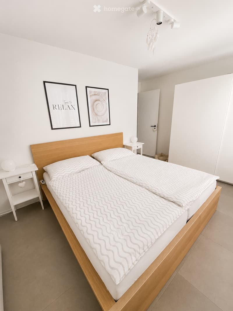 Modern bedroom with a double bed, white bedding, wooden headboard, nightstands, and decorative wall art.