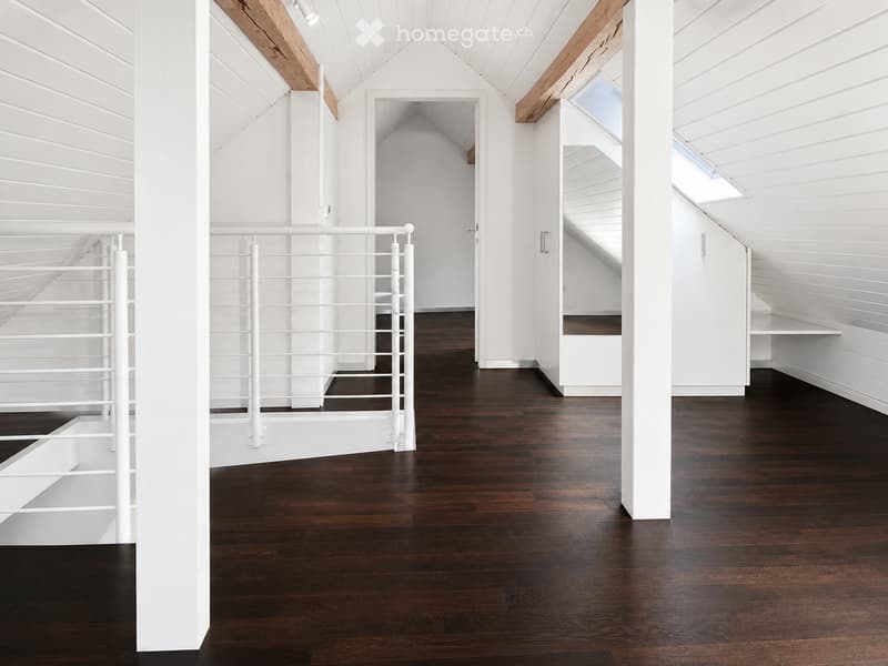 Bright, airy hallway with dark hardwood flooring, white paneled walls, and a white metal railing leading to an open area. The ceiling features exposed wooden beams and skylights, creating a modern and minimalist design.