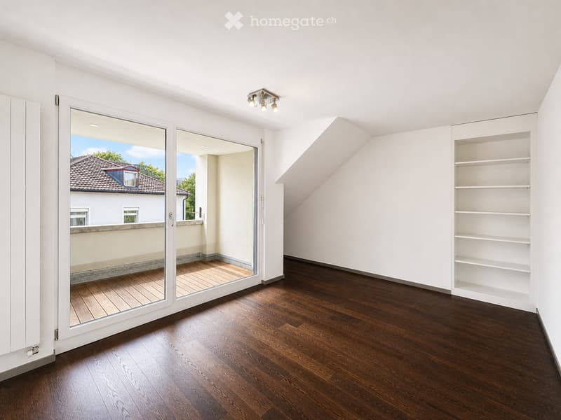 Empty room with wooden flooring, white walls, built-in shelving unit, and large sliding glass doors leading to a balcony.