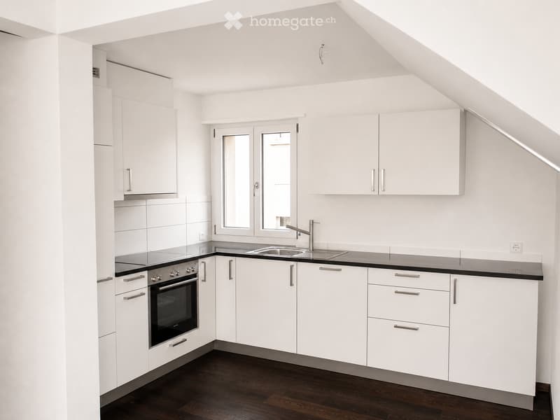 Modern kitchen with white cabinets, stainless steel appliances, and a dark wooden floor.