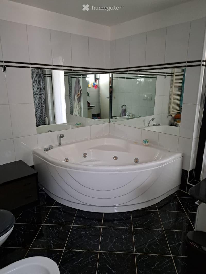 Modern bathroom with a large, curved bathtub, black marble flooring, and a large mirror above the tub.