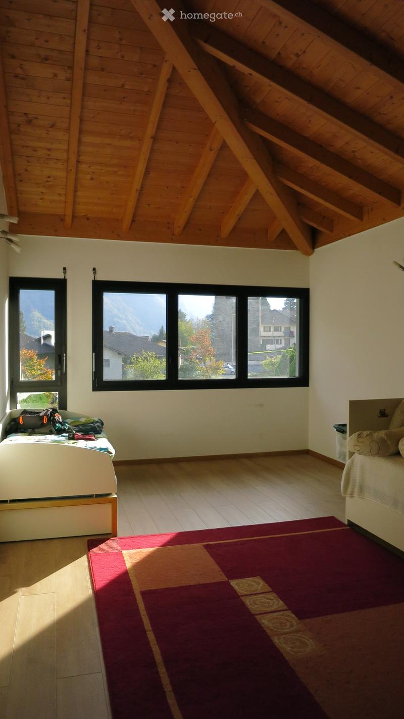 Bright bedroom with wooden slanted ceiling, large windows, tiled floor, and a colorful rug.