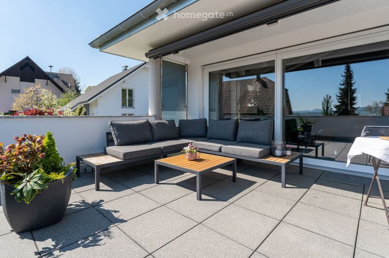 Modern outdoor patio with grey sectional sofa, wooden coffee table, small side table, and potted plants.
