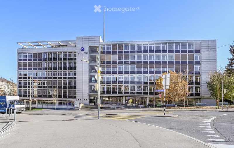 large white building, multiple windows, signage with word 'Zurich', front entrance, several benches, street light, traffic signs