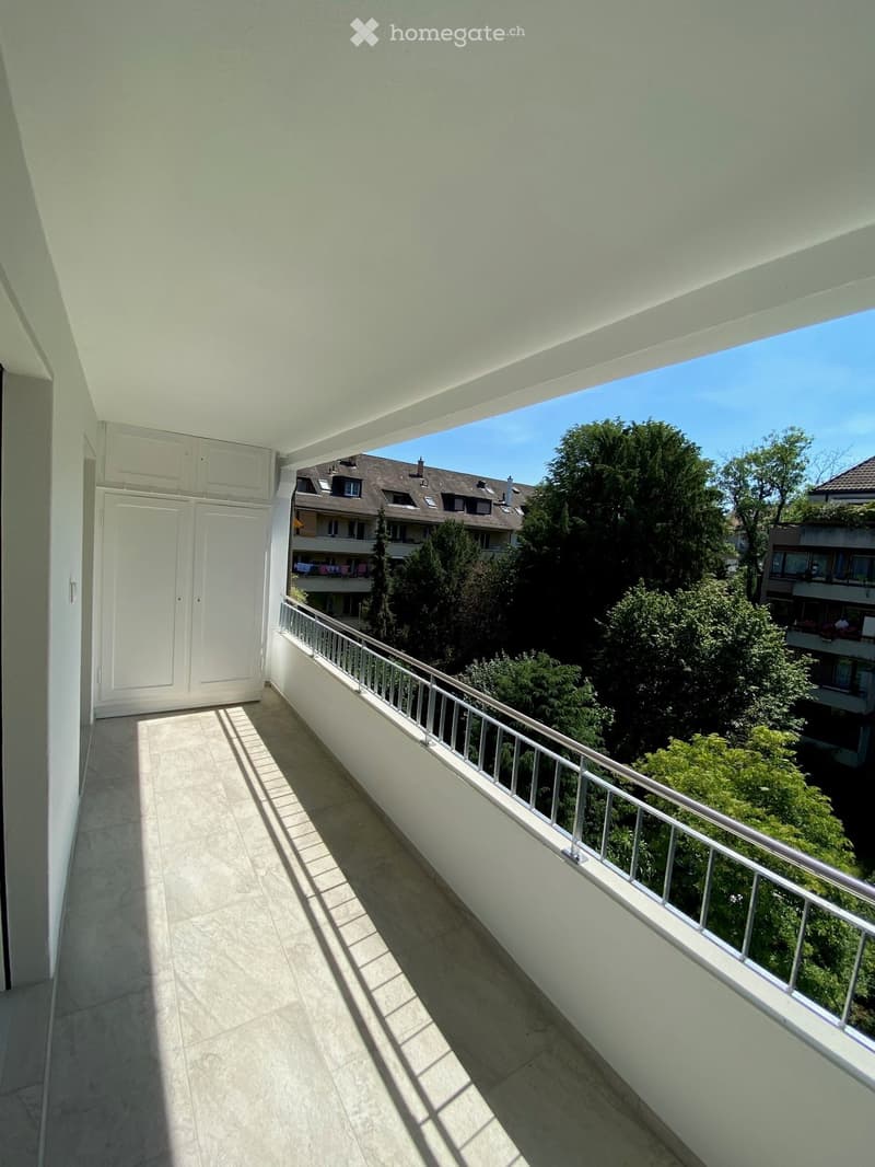 Balcony with tiled floor, white railing, and view of trees and neighboring buildings.