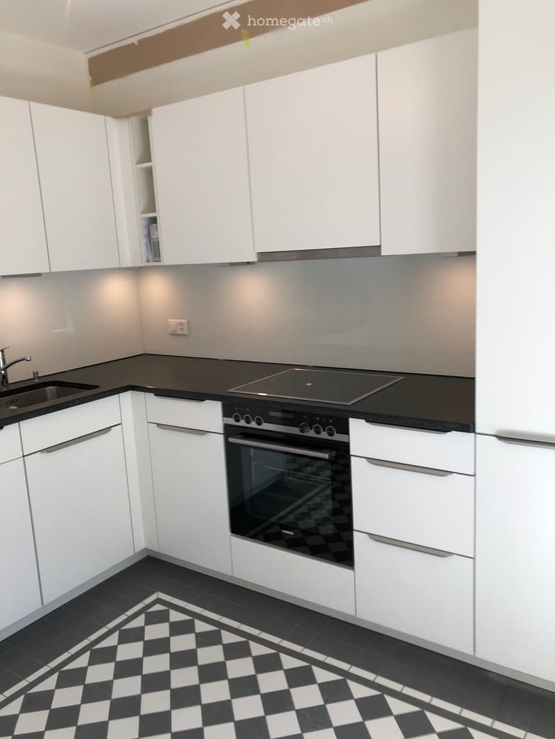 Modern kitchen with white cabinets, black countertops, and a checkered black and white tile floor. Features include a sink with a faucet, an oven, and an induction cooktop.