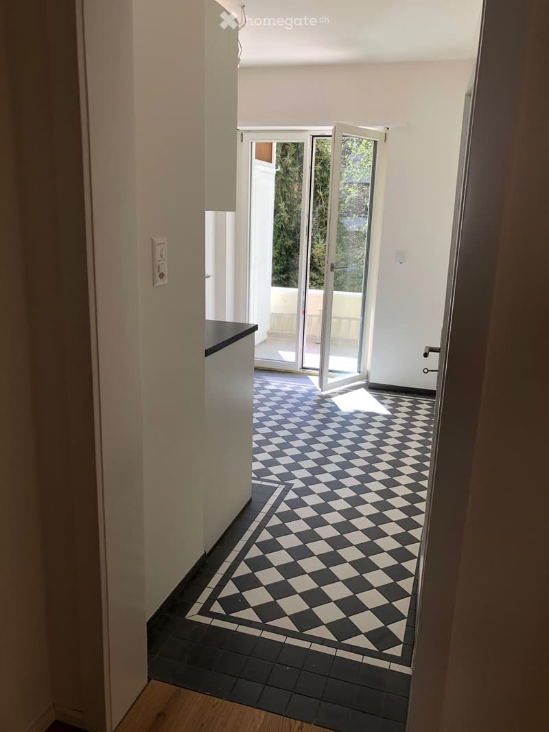 Empty hallway with black and white checkered tile floor, white walls, and sliding glass doors leading to a balcony.
