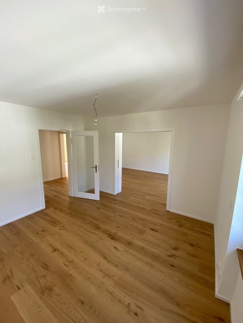 Empty room with light wooden flooring and white walls, featuring two open doorways leading to adjacent spaces.