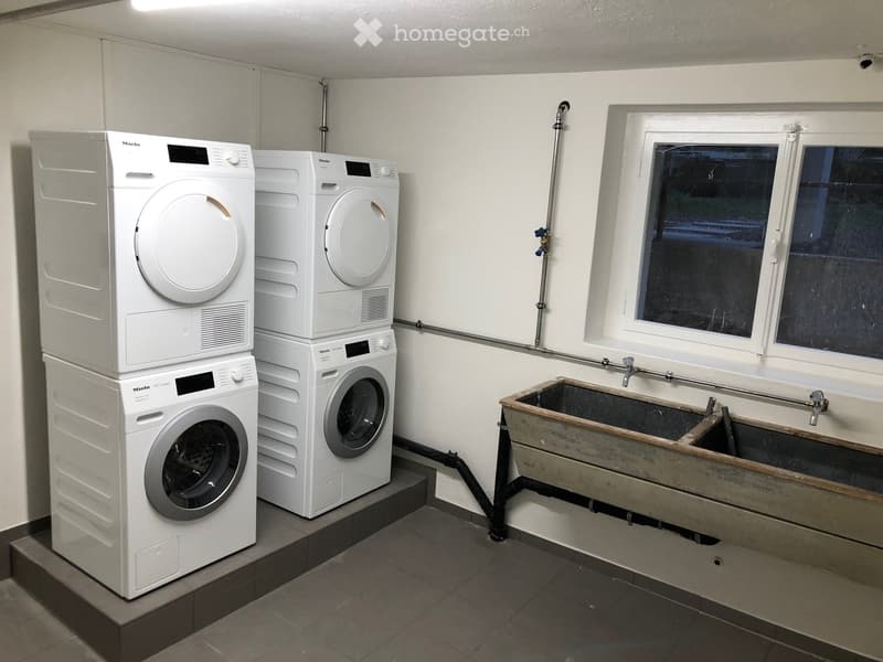 Clean, modern bathroom with two stacked washing machines and dryers, a sink, and a window for ventilation.