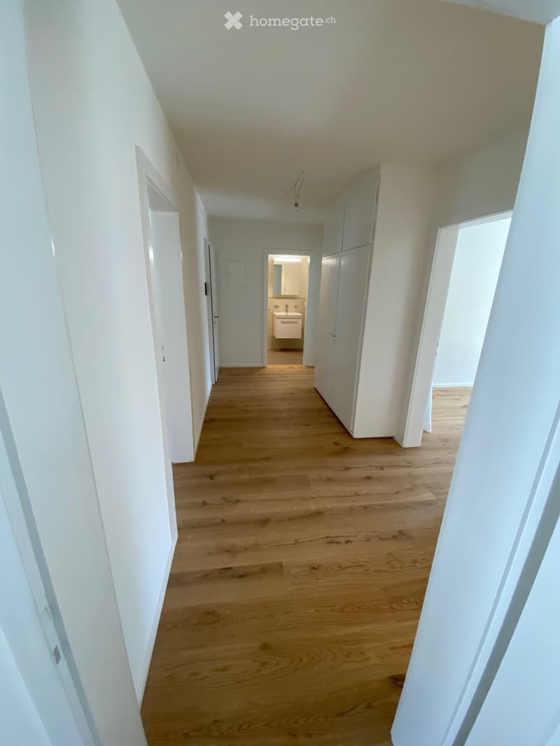 Empty hallway with wooden flooring, white walls, and several doors leading to other rooms.