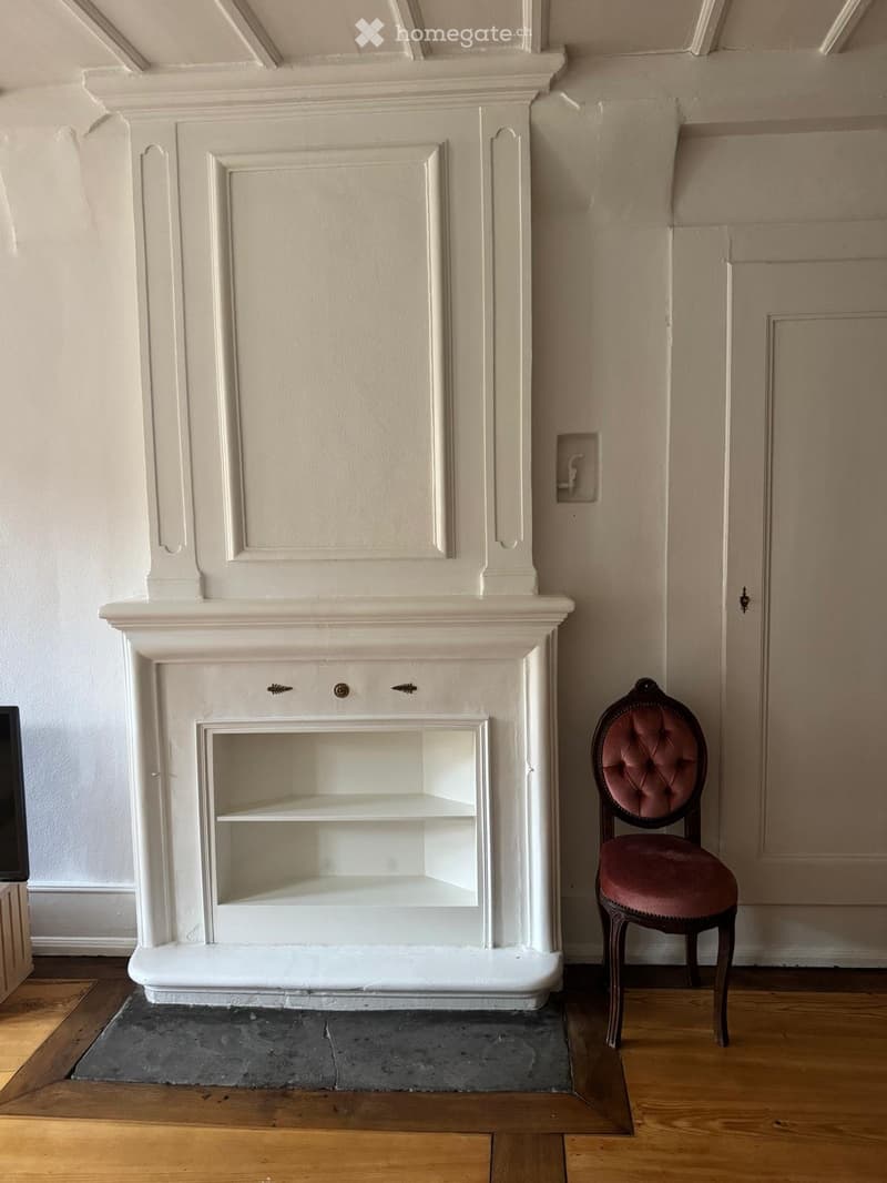 A fireplace with a built-in shelf and a single chair nearby.