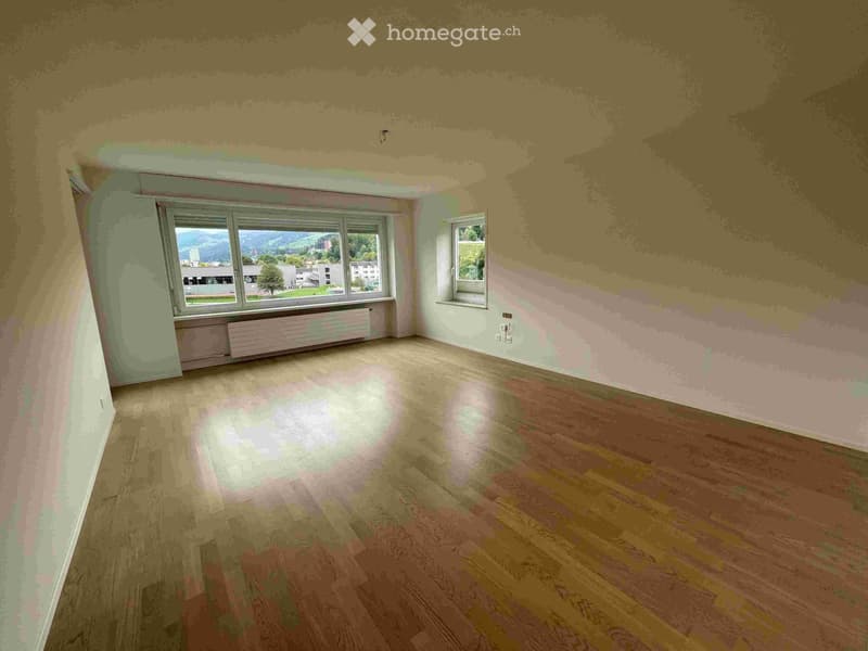 Empty room with wooden flooring, light-colored walls, and large windows offering a scenic view of the landscape.