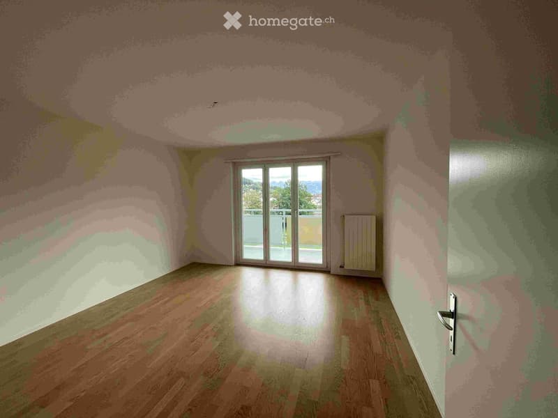 Empty room with wooden flooring, large sliding glass door leading to a balcony, and a radiator on the wall.