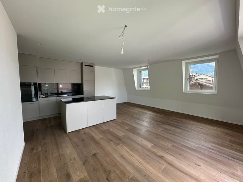 Empty kitchen with wooden flooring, white cabinets, and a black countertop. Two windows provide natural light and a view of the outdoors.