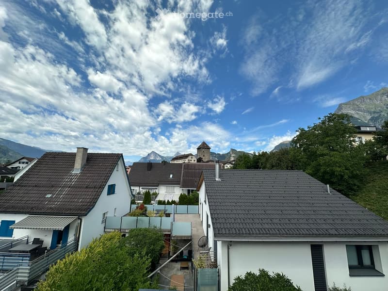 View of a residential area with several houses, surrounded by greenery and mountains in the background.