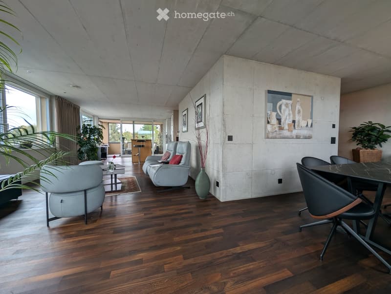 Modern living room with wooden flooring, grey leather sofa, chairs, coffee table, and a dining area with a black table and chairs.