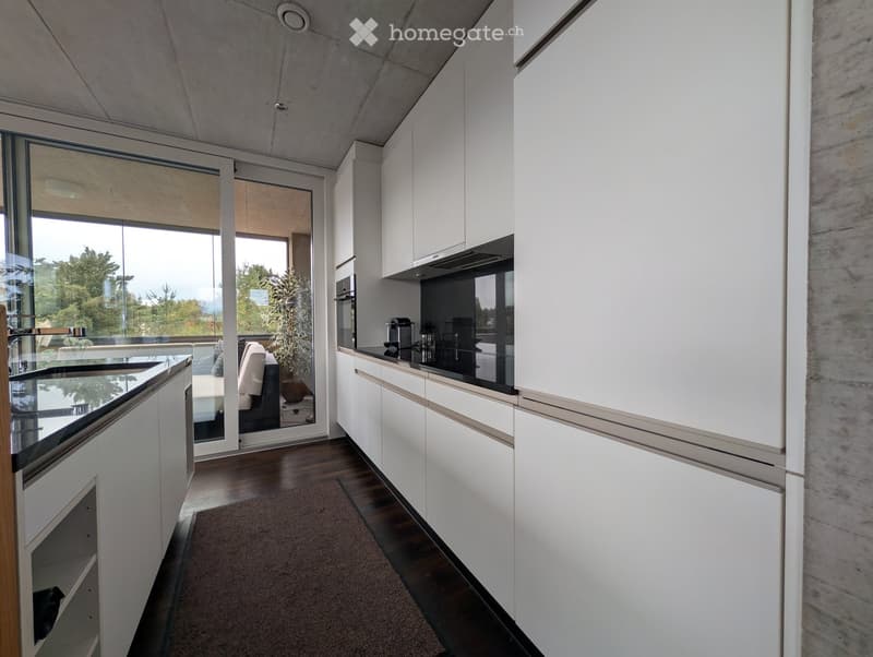 Modern kitchen with white cabinets, dark countertops, and a large window overlooking a balcony. Includes a sink, coffee maker, and oven.