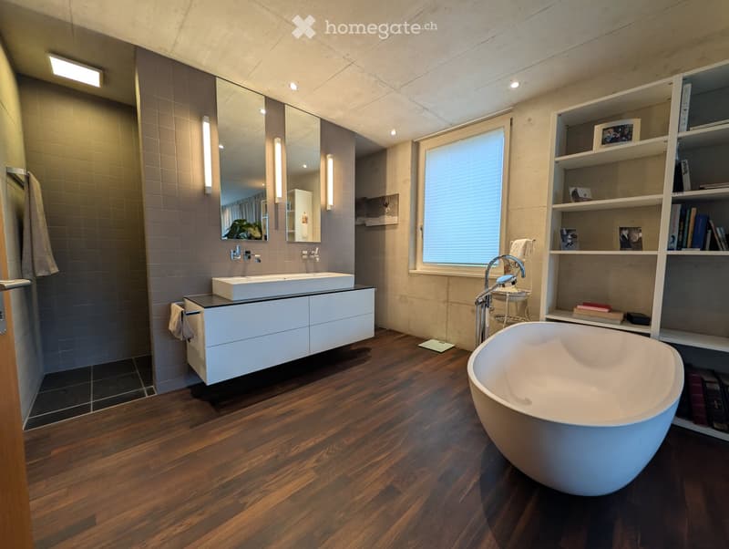 Modern bathroom with a freestanding bathtub, double sink vanity, large mirror, built-in shelving, and wooden flooring.