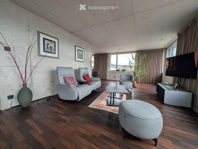 Modern living room with wooden flooring, grey leather sofa, coffee table, ottoman, chairs, vase, television, and picture frames.
