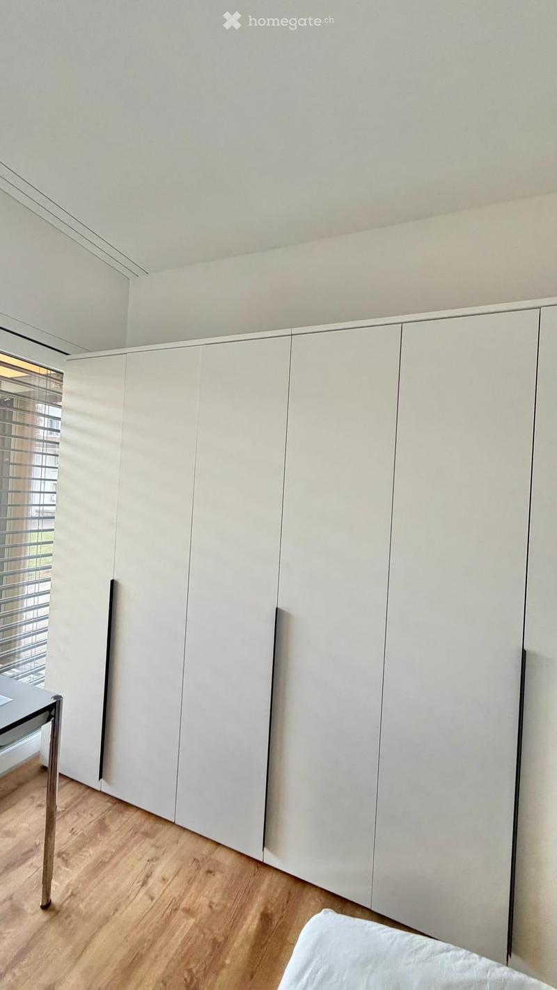 Modern, minimalist bedroom with a large white wardrobe and a small table near the window.
