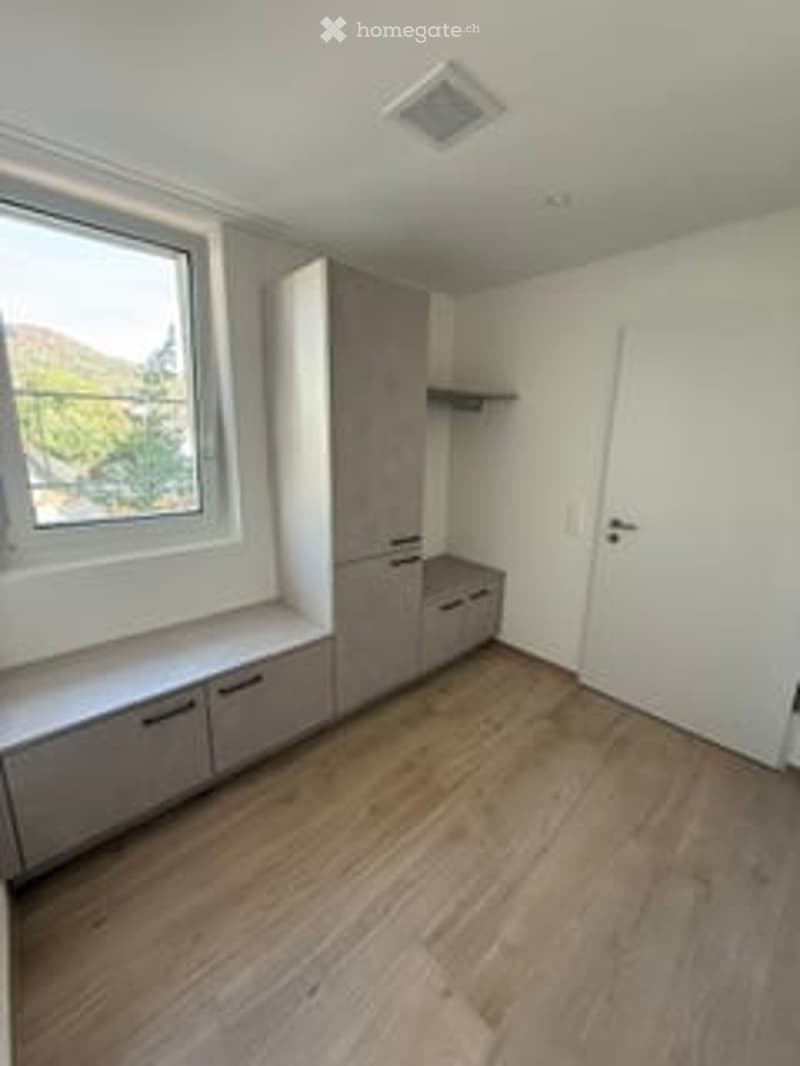 Empty room with wooden flooring, white walls, built-in cabinets, and a large window with a view.