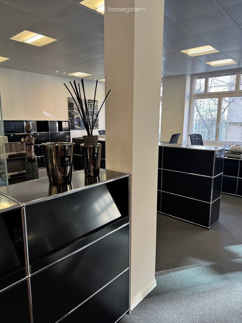 Modern office space with a sleek black reception desk, decorative vases, and chairs arranged around a table.