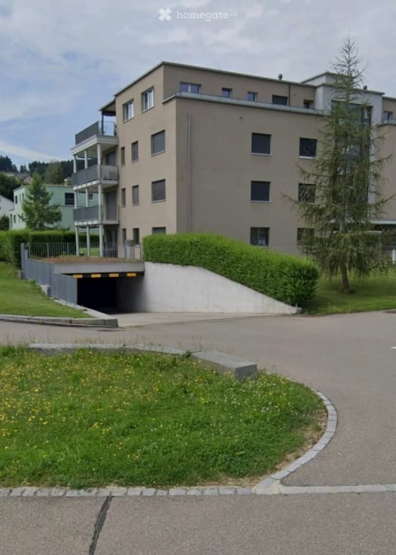 Modern two-story building with balconies, garage entrance, and landscaped surroundings.