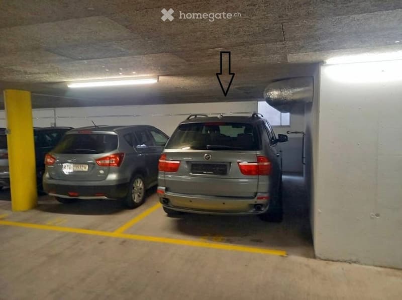 Underground parking area with several parked cars, marked parking spaces, and concrete pillars.