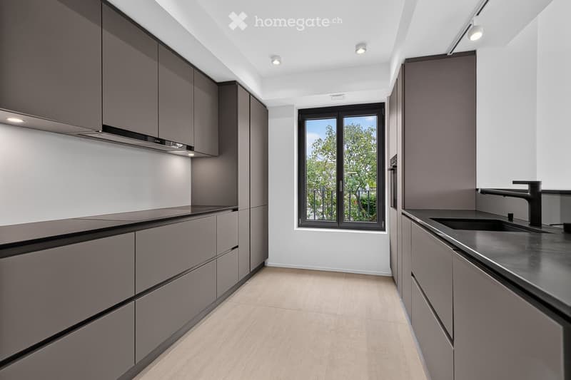 Modern kitchen with grey cabinets, a black sink, and a sleek faucet, featuring a large window with a view of greenery outside.