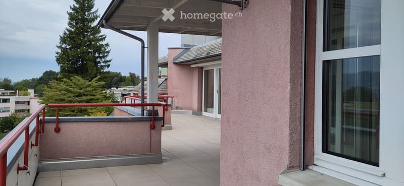Balcony with tiled floor, red metal railing, and view of greenery and neighboring buildings.