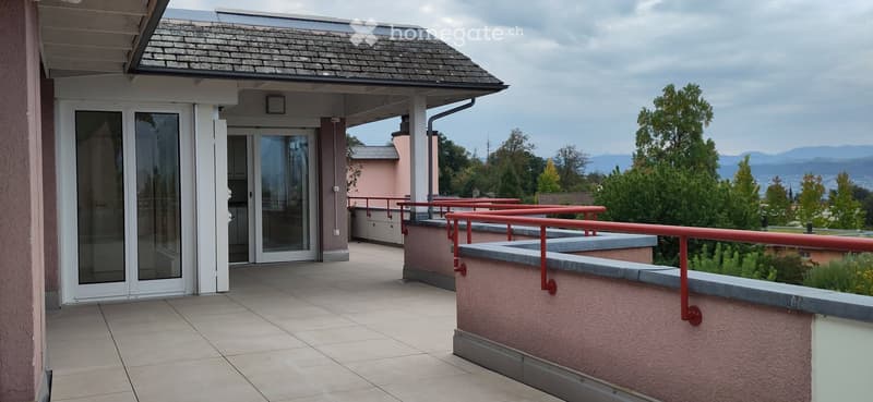 Balcony with tiled floor, red metal railings, glass doors leading to interior, scenic mountain view.