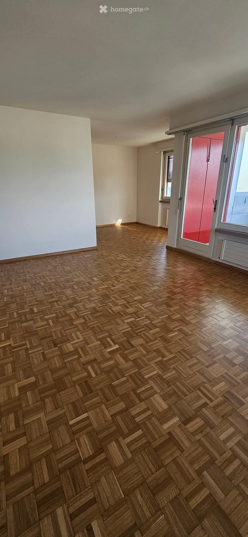 Empty room with wooden herringbone flooring, white walls, and large windows with blinds. No furniture or equipment visible.