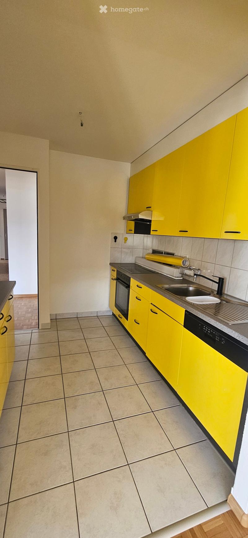Modern kitchen with yellow cabinets, tiled floor, and stainless steel appliances including a sink, oven, and dishwasher.