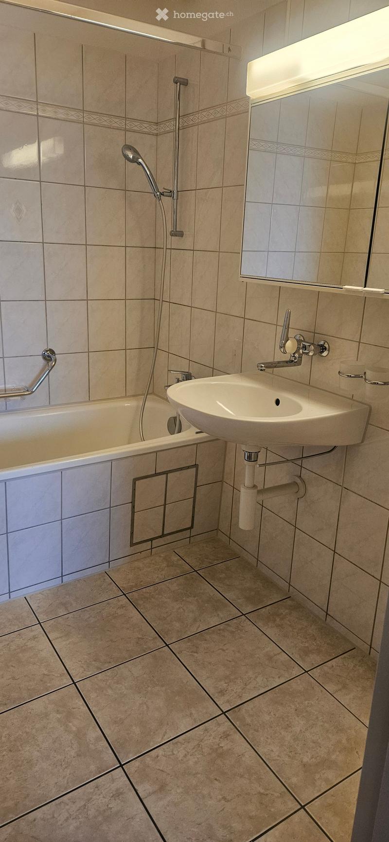 Modern bathroom with beige tiled walls and floor, featuring a bathtub, a sink with a modern faucet, and a showerhead with a handheld sprayer.