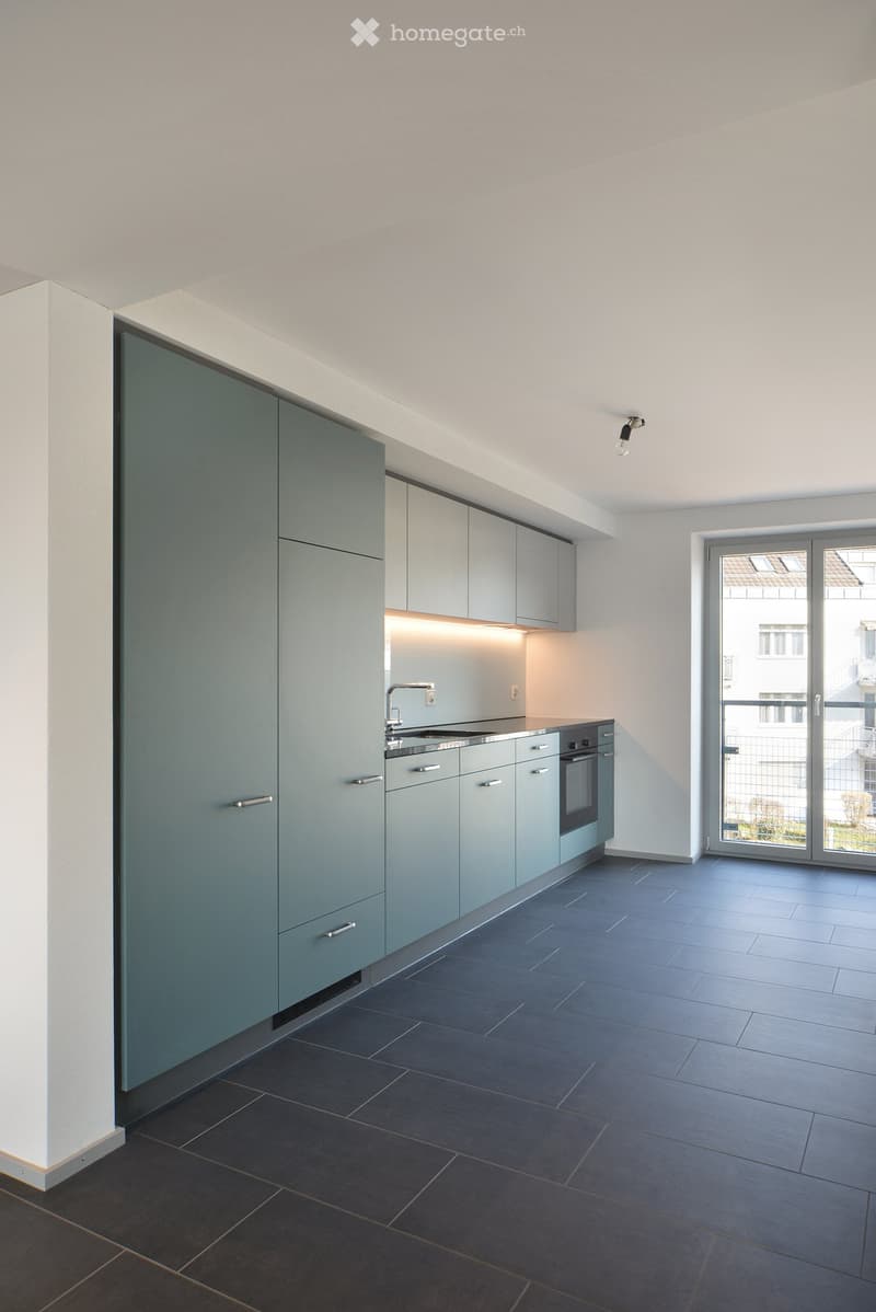 Modern kitchen with grey cabinets, dark tiled floor, and built-in appliances including a sink and oven. Features a large window and recessed lighting.