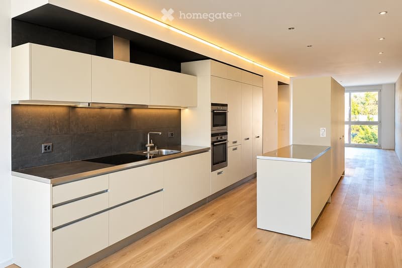 Modern kitchen with white cabinets, stainless steel appliances, and a central island. Features include a dark countertop, built-in oven, microwave, and a sleek faucet over the sink.