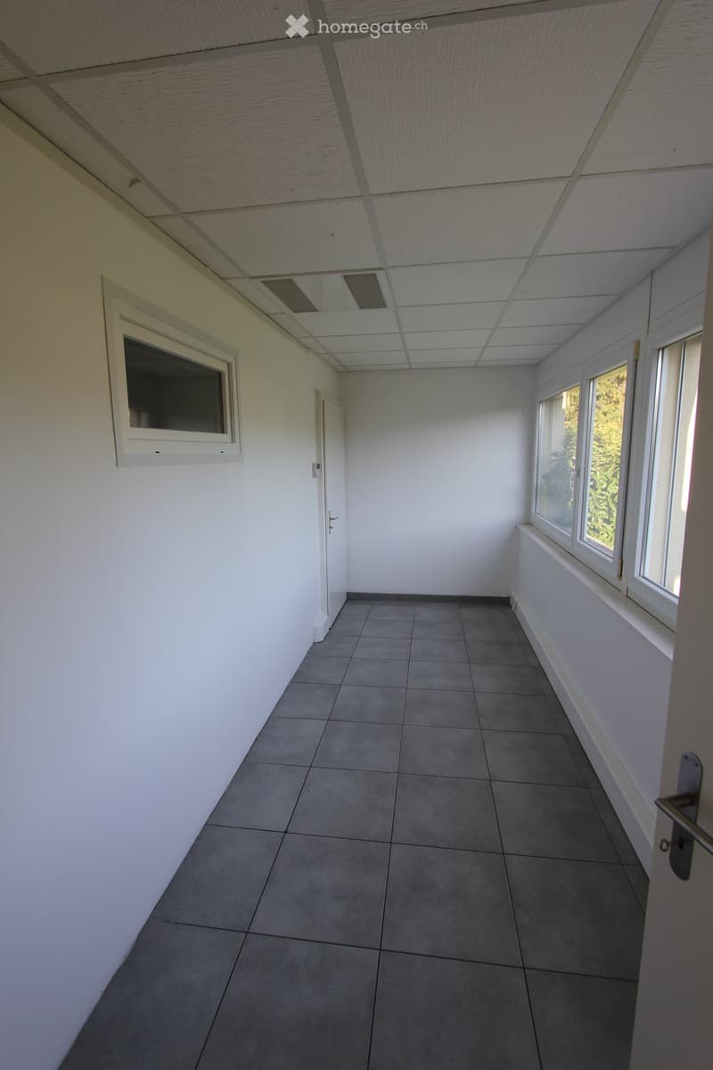 Empty room with grey tiled floor, white walls, and windows on two sides. No furniture or equipment present.