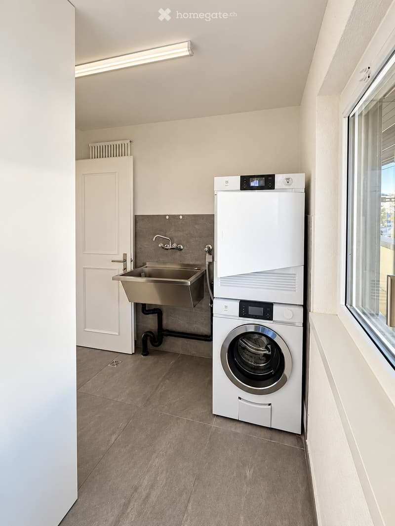 Modern, compact laundry room with a washing machine, dryer, and a stainless steel sink.