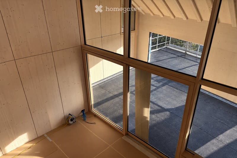 Empty room with light wooden walls and tiled floor, featuring large glass windows that open to a balcony or terrace area.