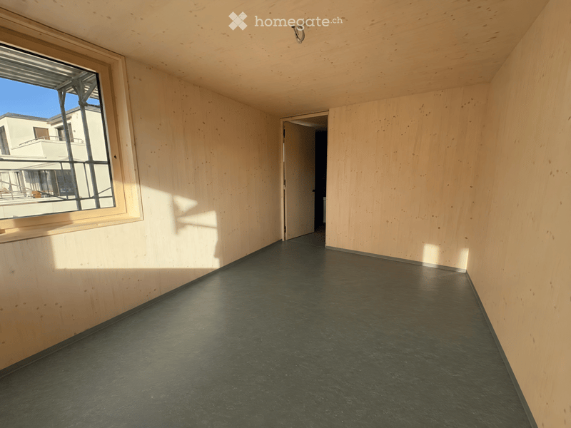 Empty hallway with wooden walls and a dark green floor, featuring a large window on one side and an open doorway at the end.