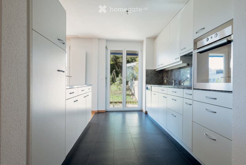 Modern kitchen with white cabinets, stainless steel appliances, dark tiled floor, and large glass doors leading to outdoor area.