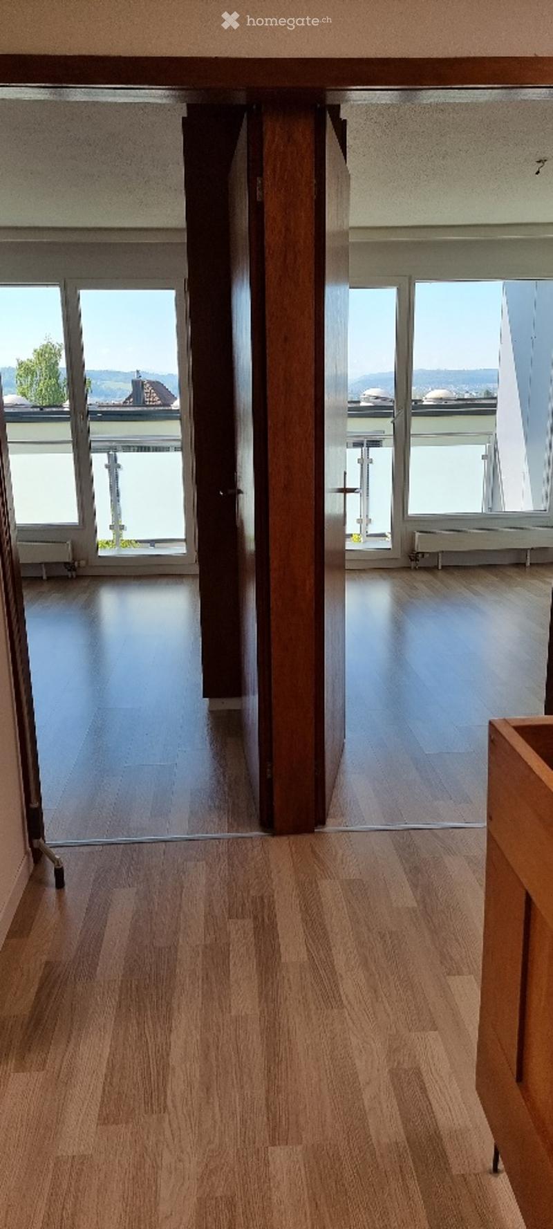 Empty room with wooden flooring, large windows, and a view of a balcony area.