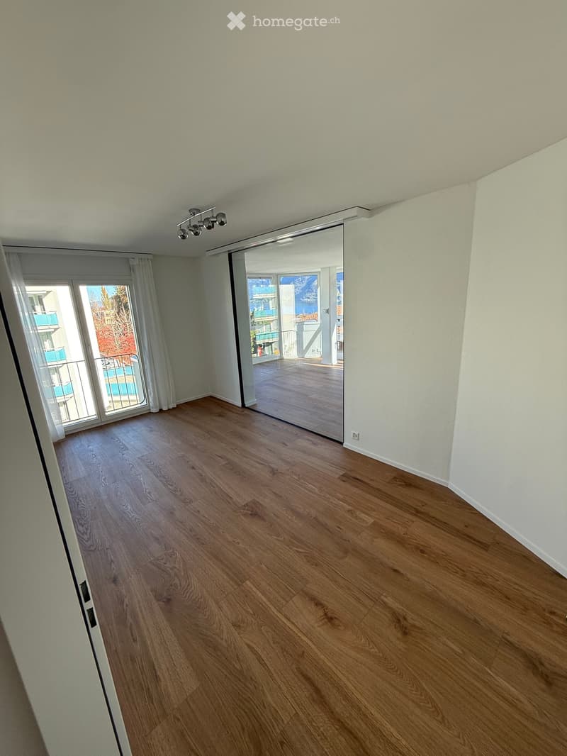 Empty room with wooden flooring, white walls, large sliding glass door leading to a balcony with a scenic view.