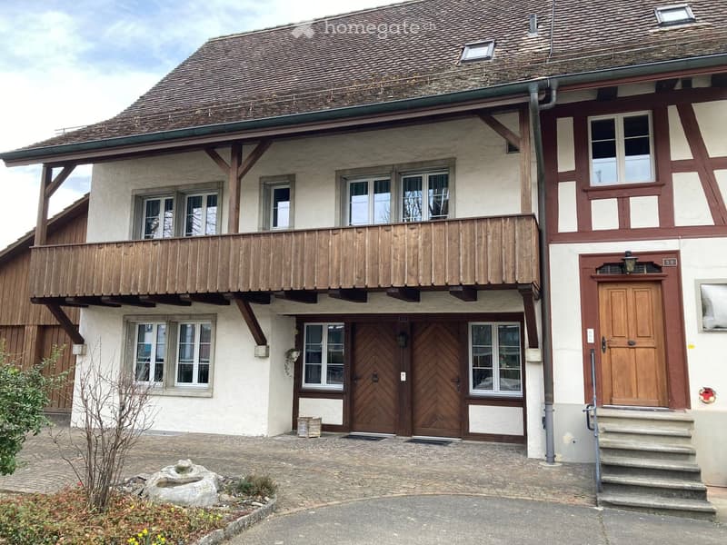 Two-story traditional house with a wooden balcony, multiple windows, and a tiled roof.