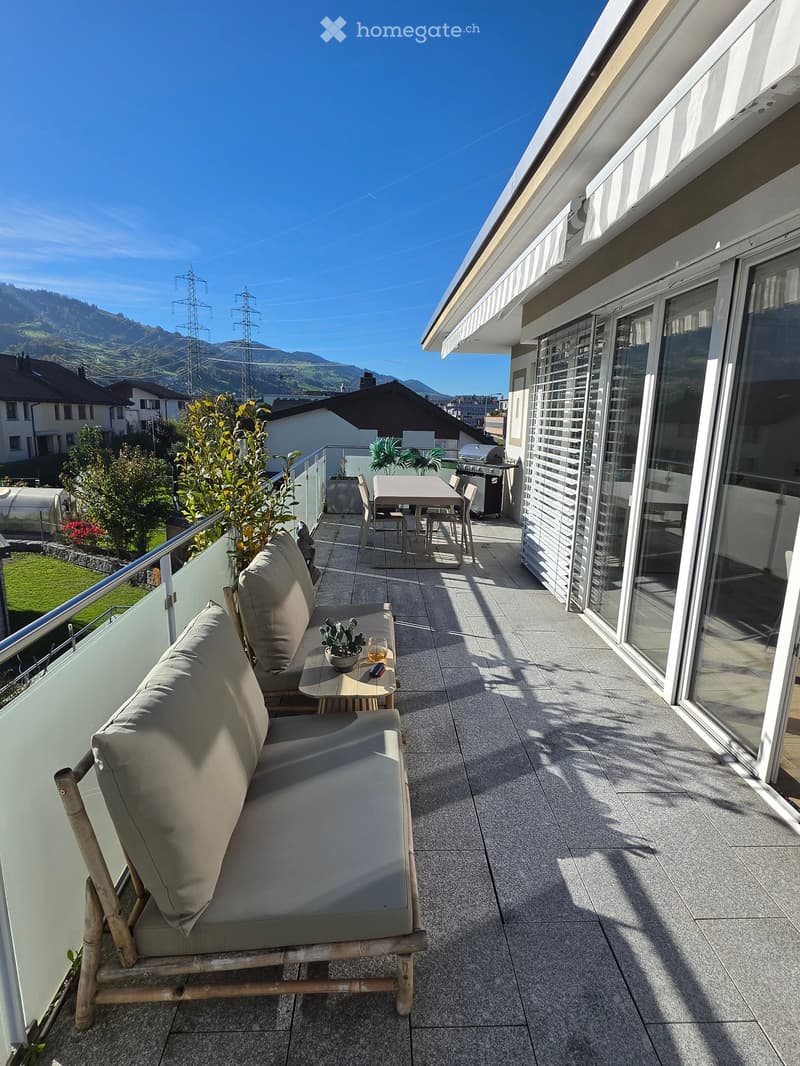 Balcony with a sofa, small table, chairs, and potted plants, overlooking a scenic mountain view.