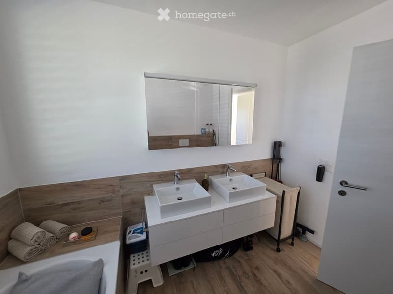 Modern bathroom with double sink vanity, large mirror, wooden accents, and neatly arranged towels and bathrobe.
