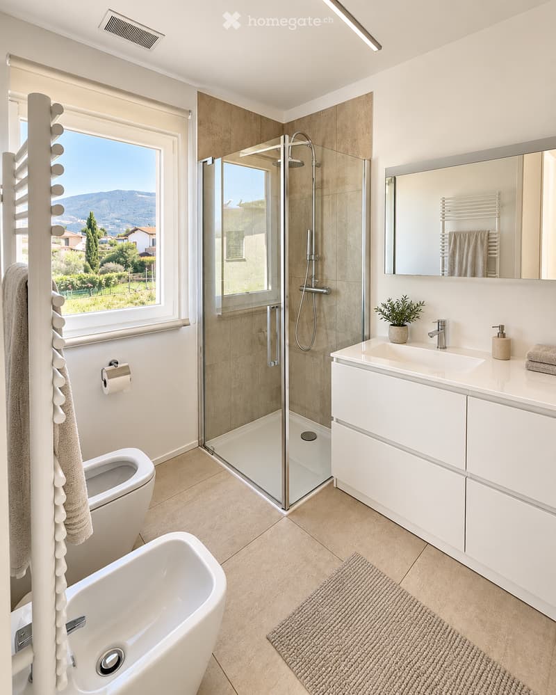 Modern bathroom with a bathtub, toilet, sink, and glass-enclosed shower. Features a large window with a scenic view, a towel rack, and a small plant on the sink counter.