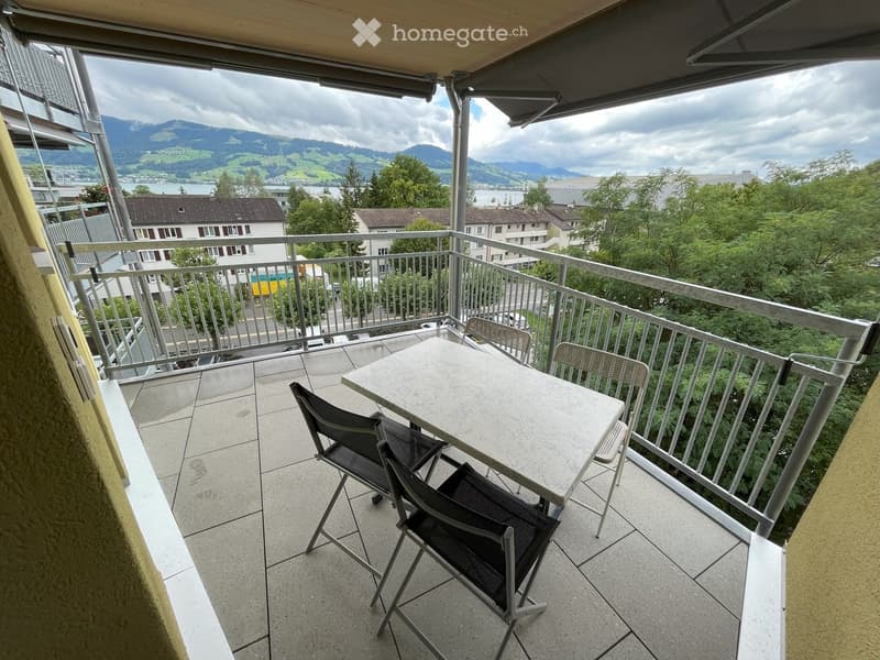 Balcony with a table and chairs, overlooking a scenic landscape with mountains and a lake.
