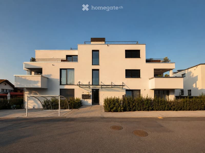 Modern two-story house with white facade, large windows, balconies, and a covered entrance area.