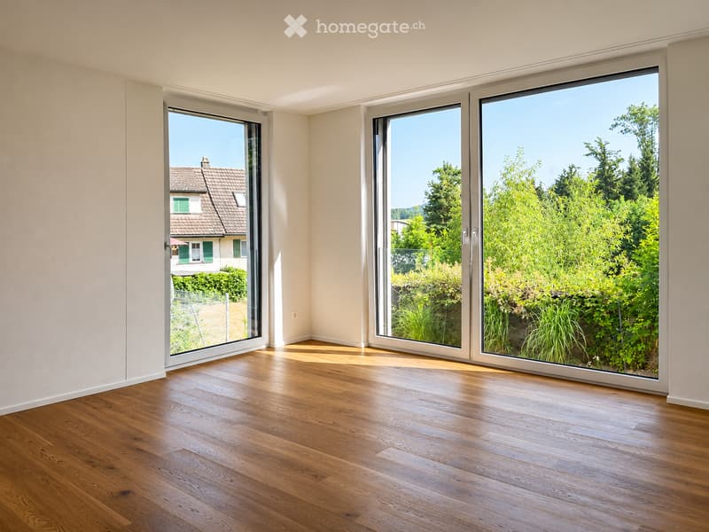 Empty room with wooden flooring and large glass sliding doors leading to a garden view.